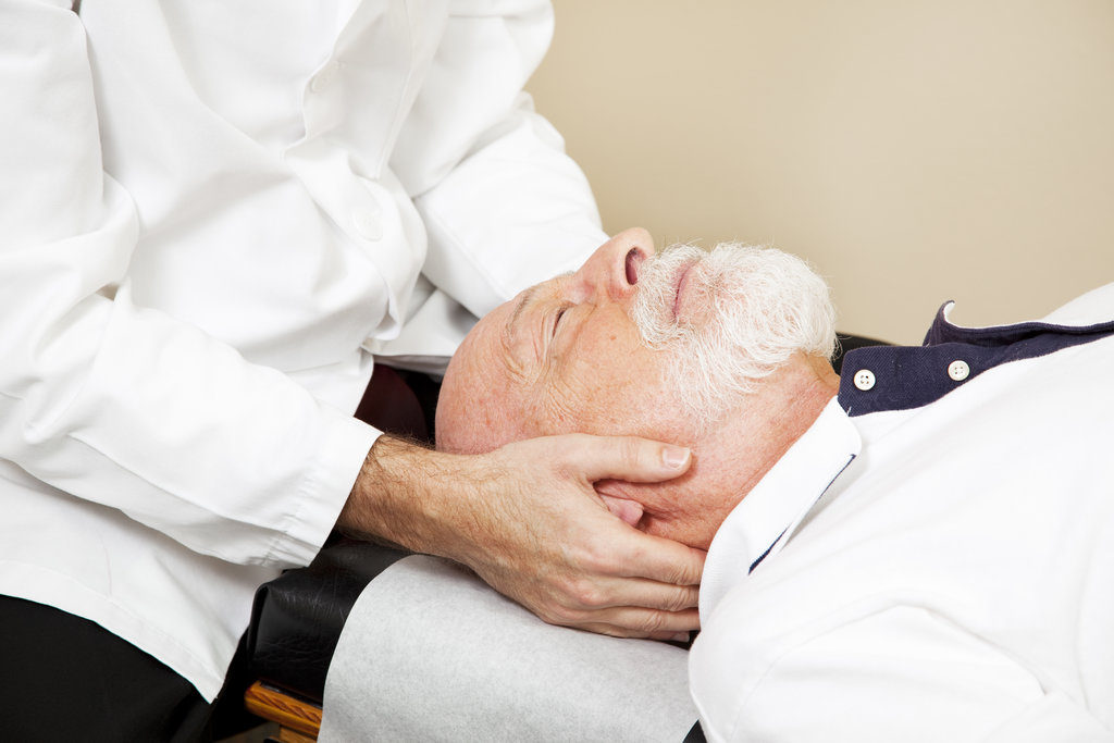 Closeup of a chiropractor adjusting a senior patient's cervical spine (neck).